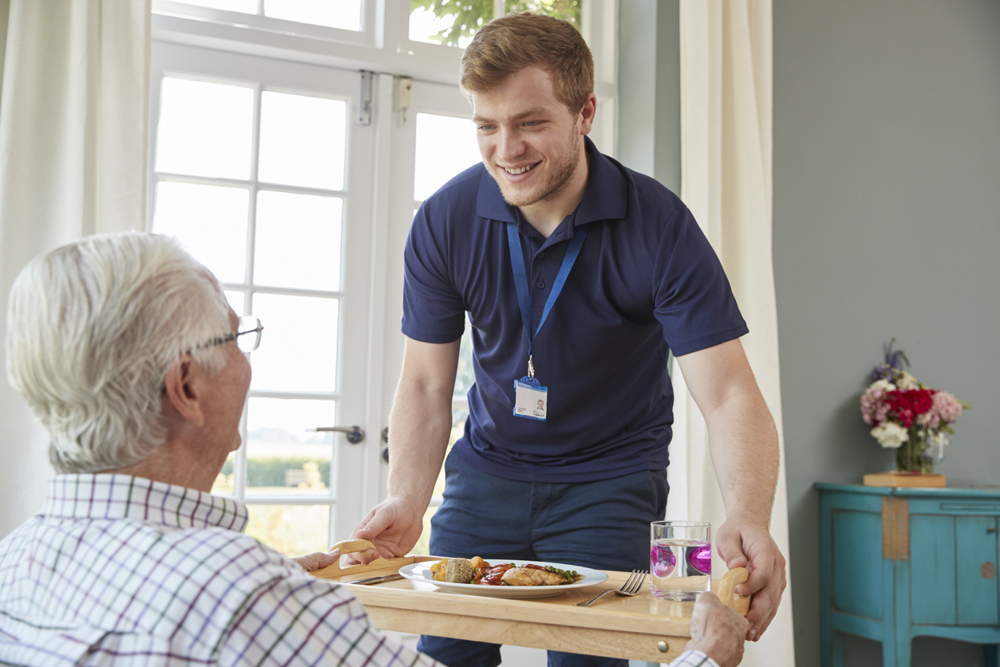 Male care worker serving food to a senior man