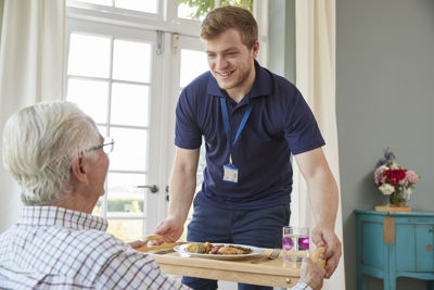 Male care worker serving food to a senior man