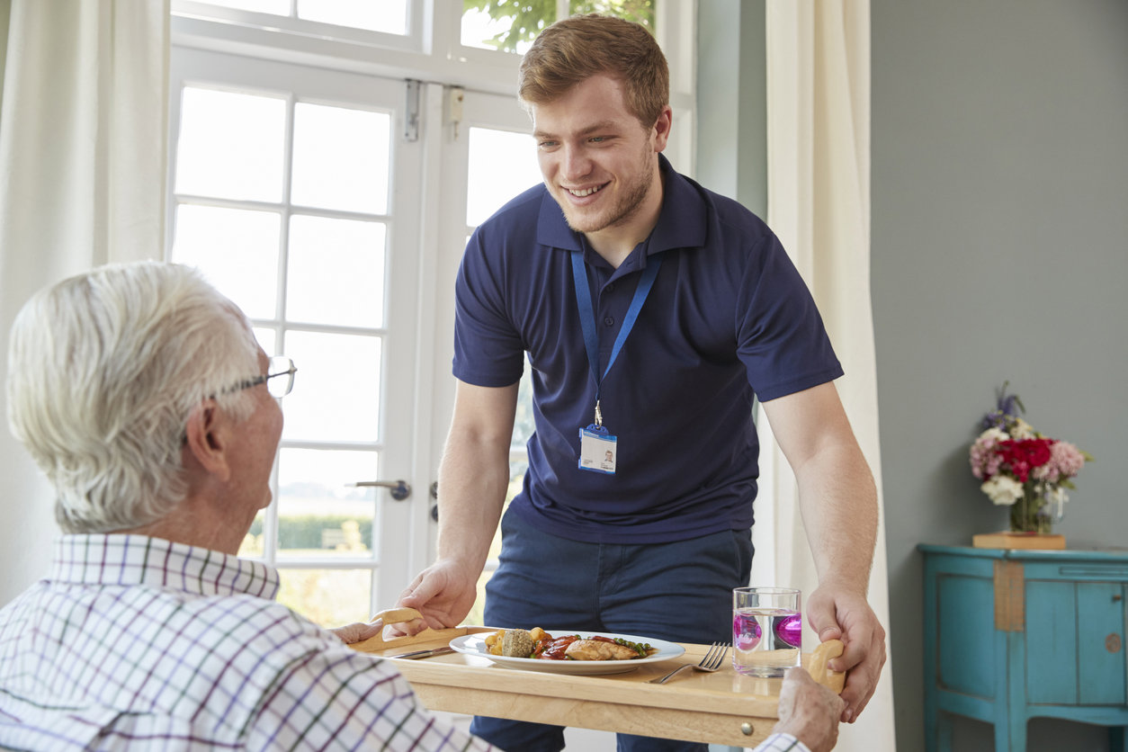 Male care worker serving food to a senior man