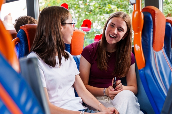 Two Girls Smiling And Talking To Each Other On A Bus