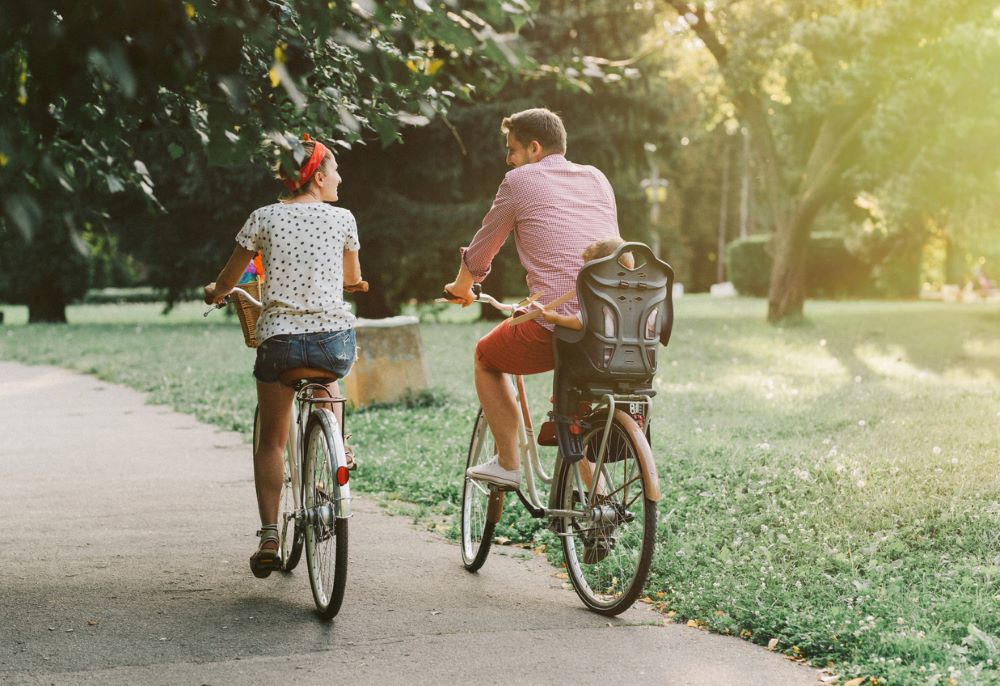 Couple riding through a park with a child on the back of the bike