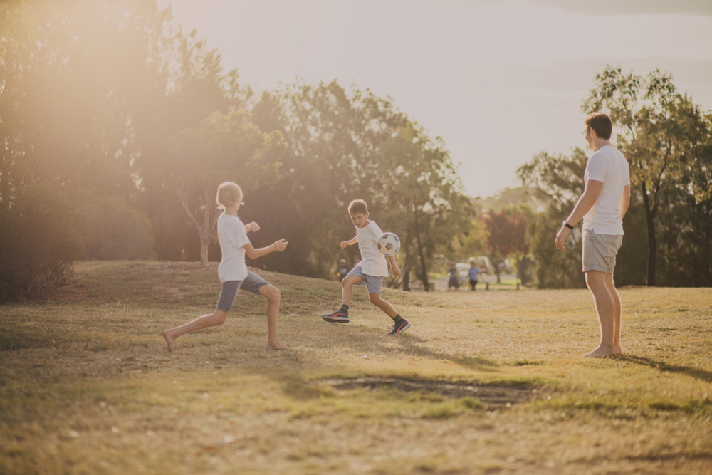 Children in park playing football with their dad