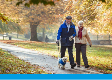 Older couple walking the dog through a park