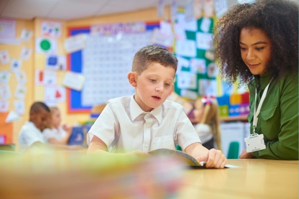 Child reading in classroom with teacher helping him