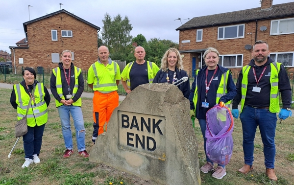 A group of men and women in hi-vis vests by a sign reading Bank End at the Worsbrough clean-up