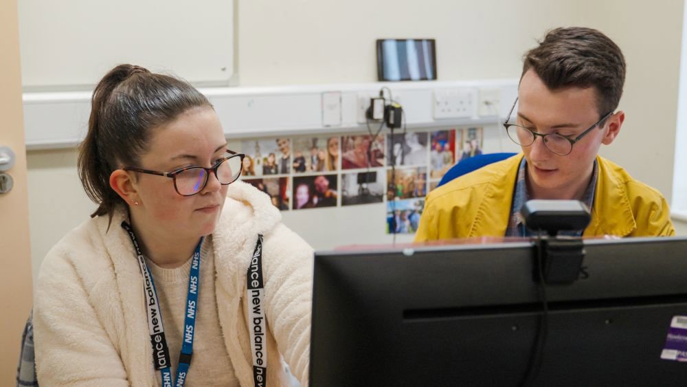 Two people sat at desk with computer