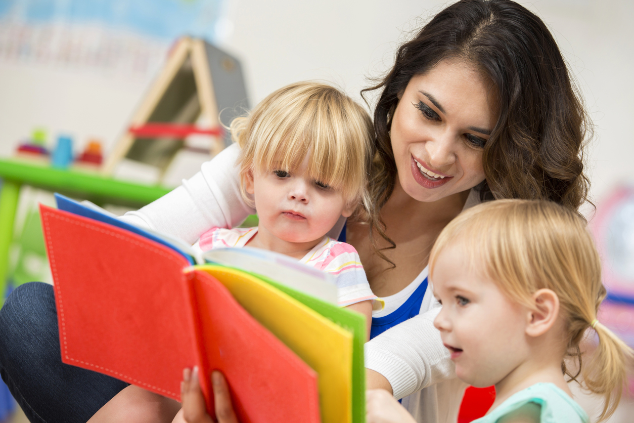 Two little girls reading with adult
