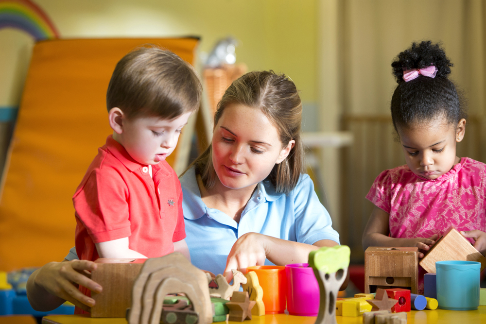Nursery teacher supervising children playing with blocks