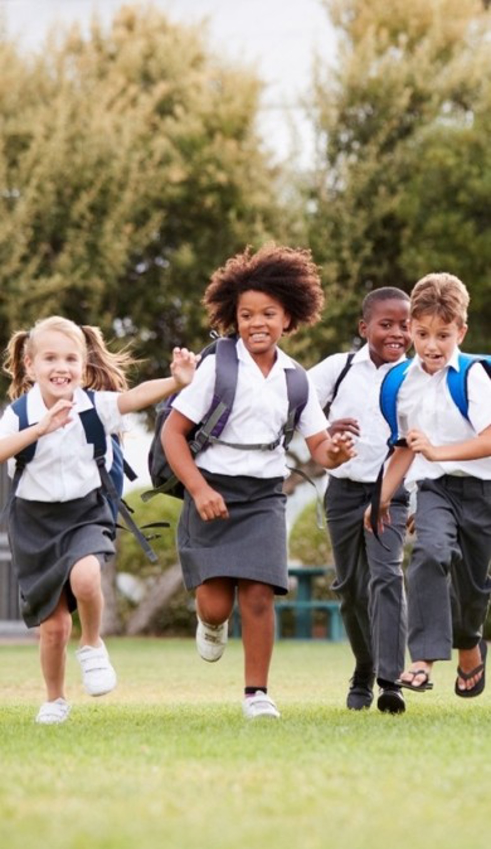 Group Of School Children In Uniform Running Across A Field