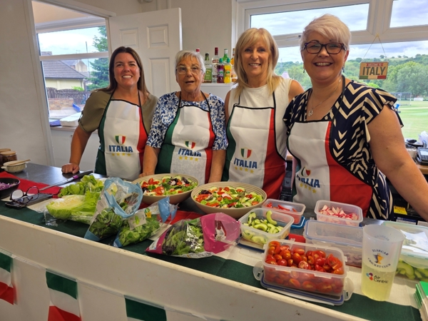 A group of smiling women serving Italian food at Elsecar cricket club