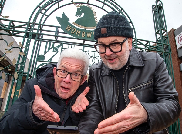 Two Men In Glasses Looking At A Phone In Front Of A Sign Saying Wombwell