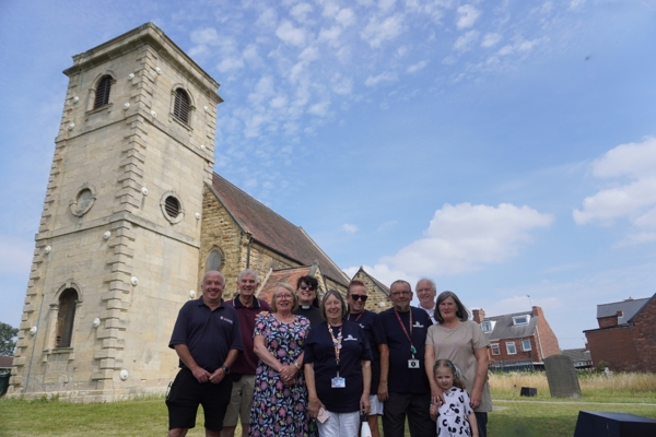 A group of people smiling in front of a church with a tower at St Helen's Church in Thurnscoe