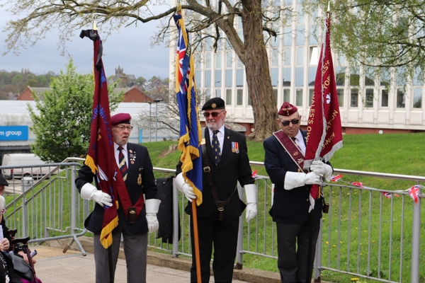 Photograph of three individuals in ceremonial attire hold large flags during ceremony.jpg