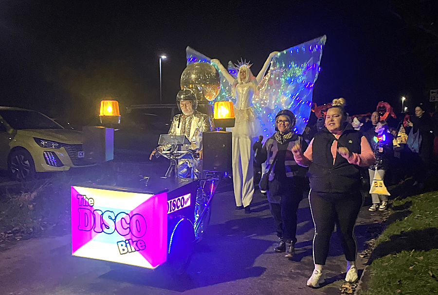People Holding Lanterns In A Parade Led By A Disco Bike (1) People Holding Lanterns In A Parade Led By A Disco Bike (1)