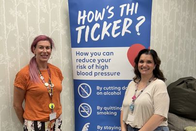 Two women standing by a banner reading How's Thi Ticker.jpg