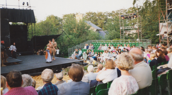 Rows Of People Watch A Performance On A Black Stage In An Open Air Theatre For The Worsbrough Mystery Plays